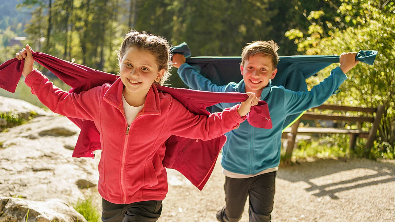 Ein Mädchen und  ein Junge  rennen mit wehender Jacke einen Berg hinauf